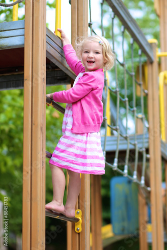 Happy kid enjoying active summer vacation. Adorable little child, blond cute toddler girl, having fun outdoors climbing on playground in the park on a sunny day