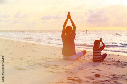 father and son doing yoga at sunset sea