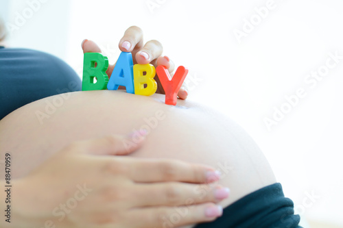 Young expectant mother with letter blocks spelling baby on her pregnant belly
