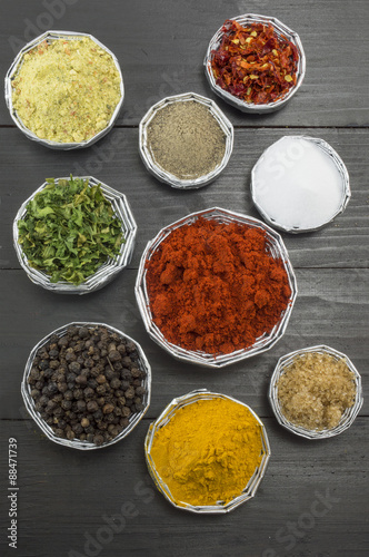 Various spices in shiny bowls on a dark wooden table
