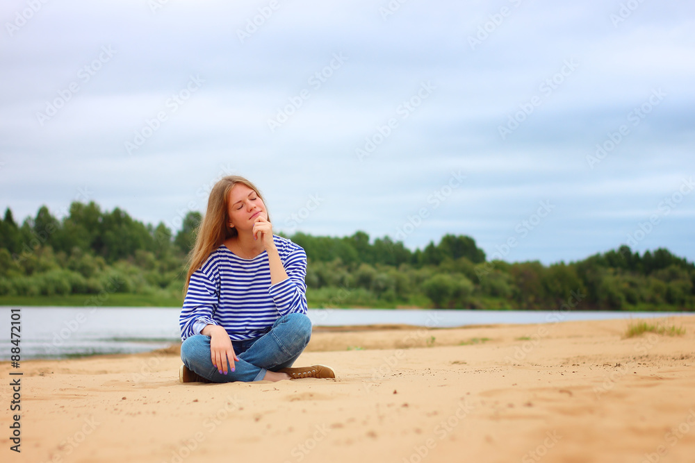 Beautiful young girl sitting on the beach, smiling, resting, enjoying a sunny summer day