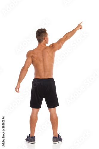 Rear view of muscular man standing with arms raised and pointing up. Full length studio shot isolated on white.
