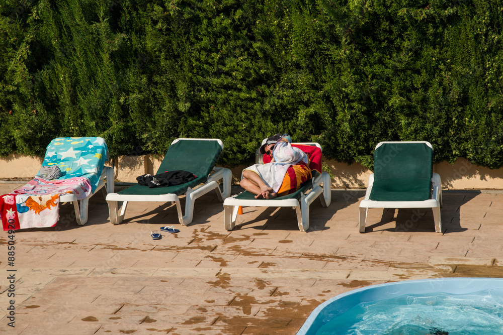 Un homme se cache sous sa serviette, allongé sur un transat au bord d'une  piscine Photos | Adobe Stock