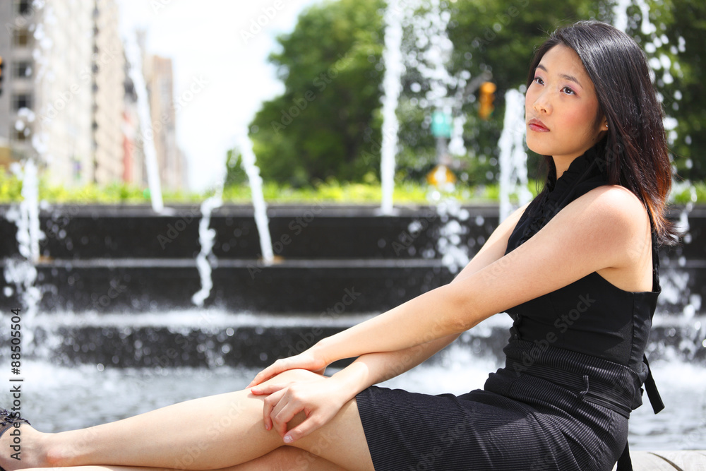 A daydreaming woman seated in front of a city fountain.