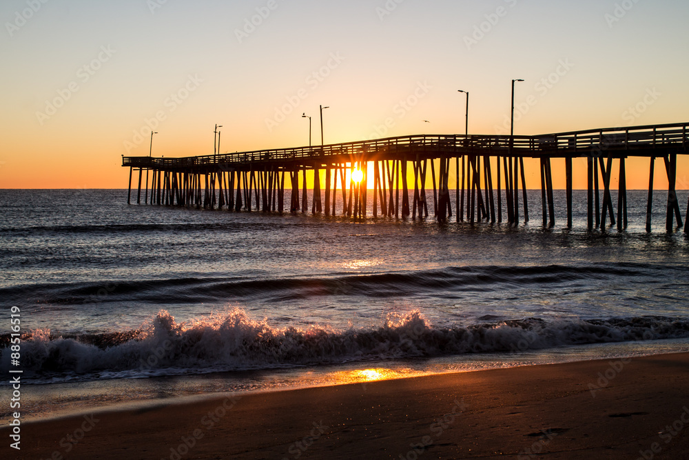 Sunrise with the Virginia Beach fishing pier in silhouette with waves crashing in foreground