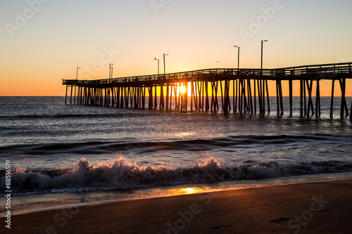 Sunrise with the Virginia Beach fishing pier in silhouette with waves crashing in foreground