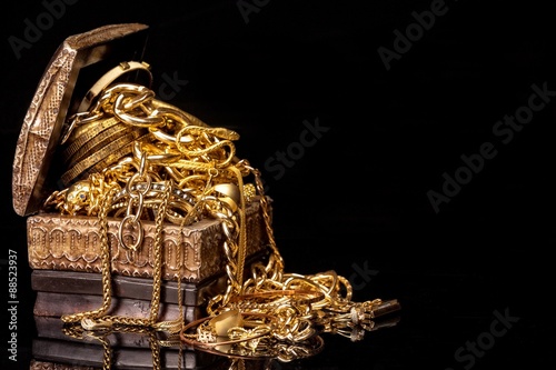 Old wooden chest with pile of various golden jewelry, isolated against black background.
