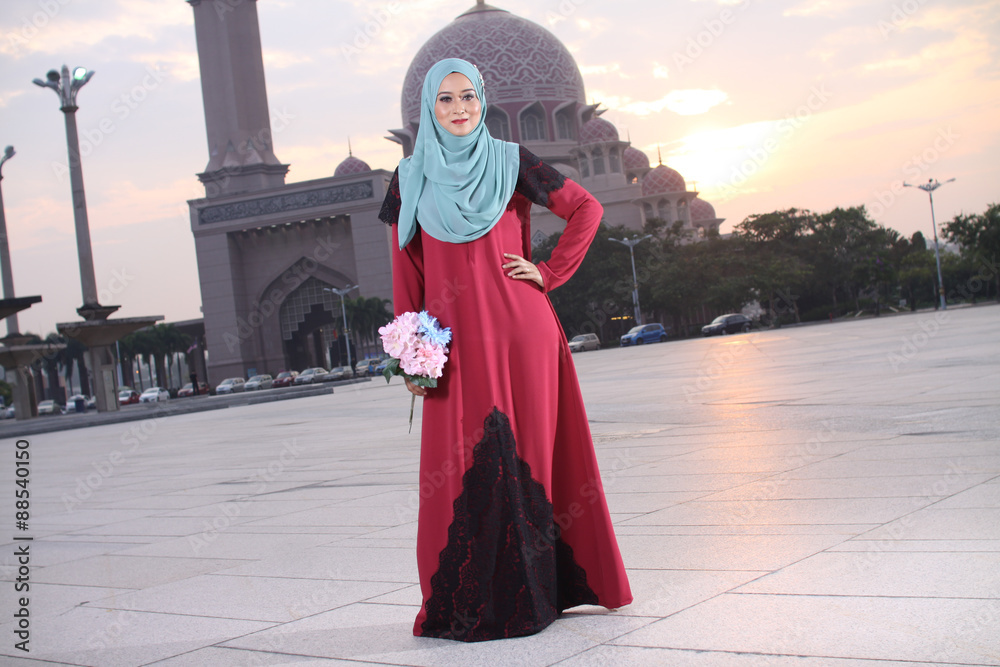 high fashion muslim women holding a flower with mosque background at sunset high fashion muslim women holding a flower with mosque background at sunset