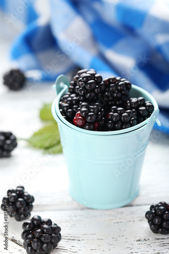 Beautiful ripe blackberry in bucket on white wooden background