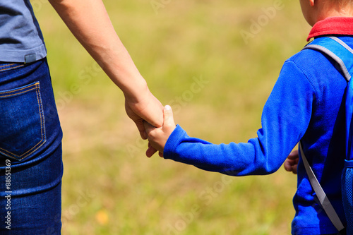 Mother holding hand of little son with backpack outdoors