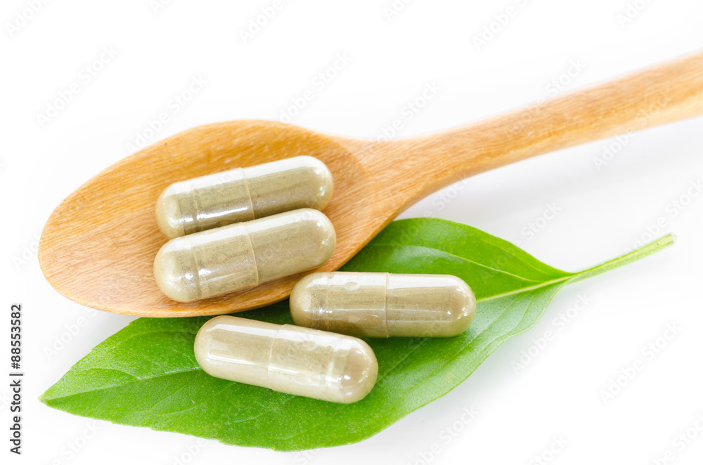 Yellow herb capsule with green leaf in wooden spoon. Yellow herb capsule with green leaf in wooden spoon.