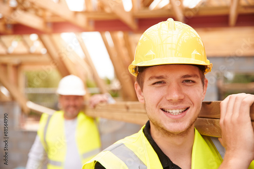 Builder And Apprentice Carrying Wood On Construction Site