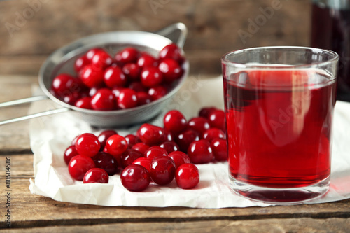 Glass with cherry juice on table, on wooden background