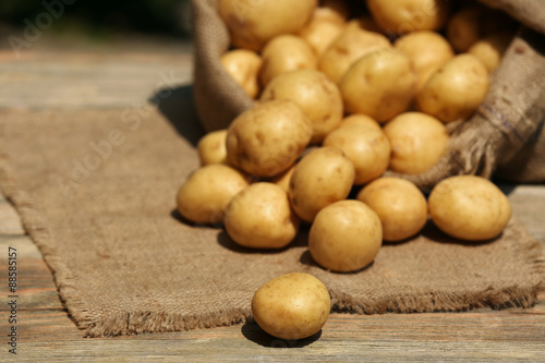 New potatoes in sackcloth bag on wooden table, closeup