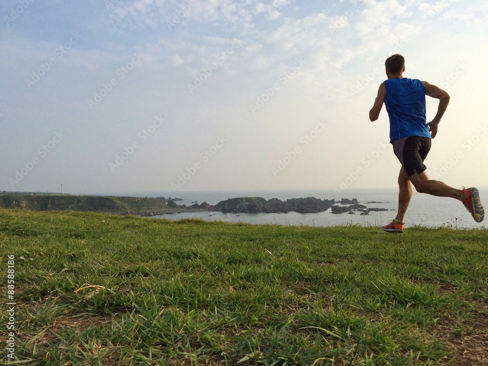 Runner on grassy cliff top trail with sea in background - obrazy, fototapety, plakaty 
