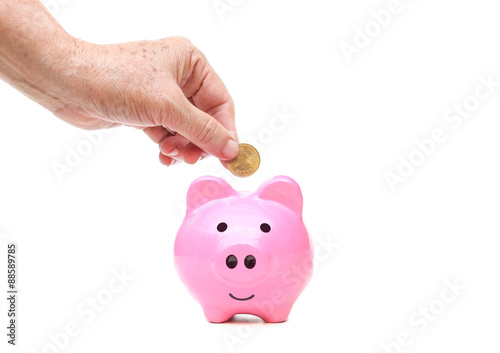 old female elderly hand putting a golden coin into a saving piggy bank - saving money for retirement concept