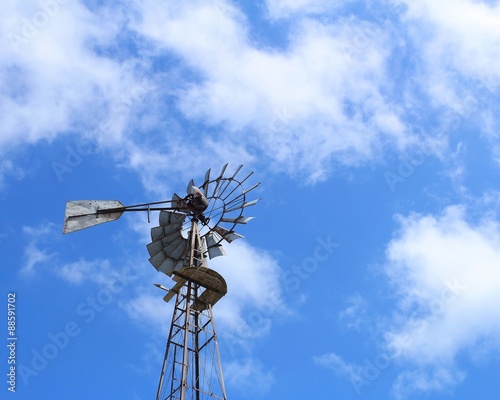 Vintage windmill with cloudy blue sky in background.