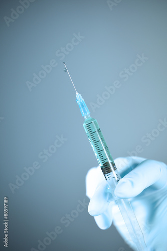 Medical syringe in hand with white glove on gray background take with art lighting and blue filter