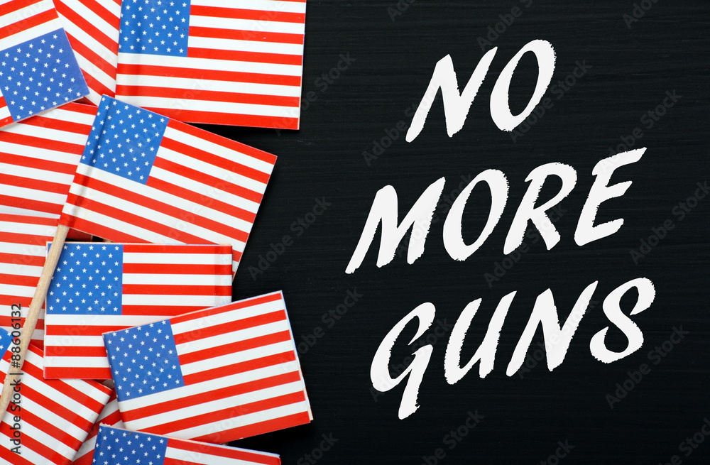 Obraz premium The phrase No More Guns in white text on a blackboard next to flags of the United States of America as a call for gun control