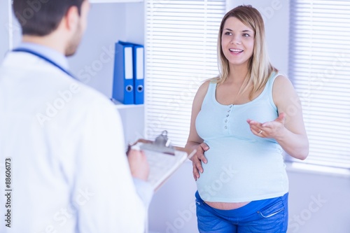 Smiling pregnant patient talking to doctor which is taking notes