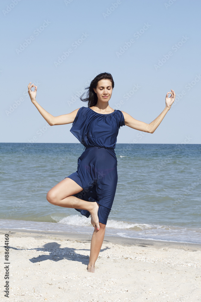 Young beautiful woman doing yoga at seaside in blue dress Young beautiful woman doing yoga at seaside in blue dress