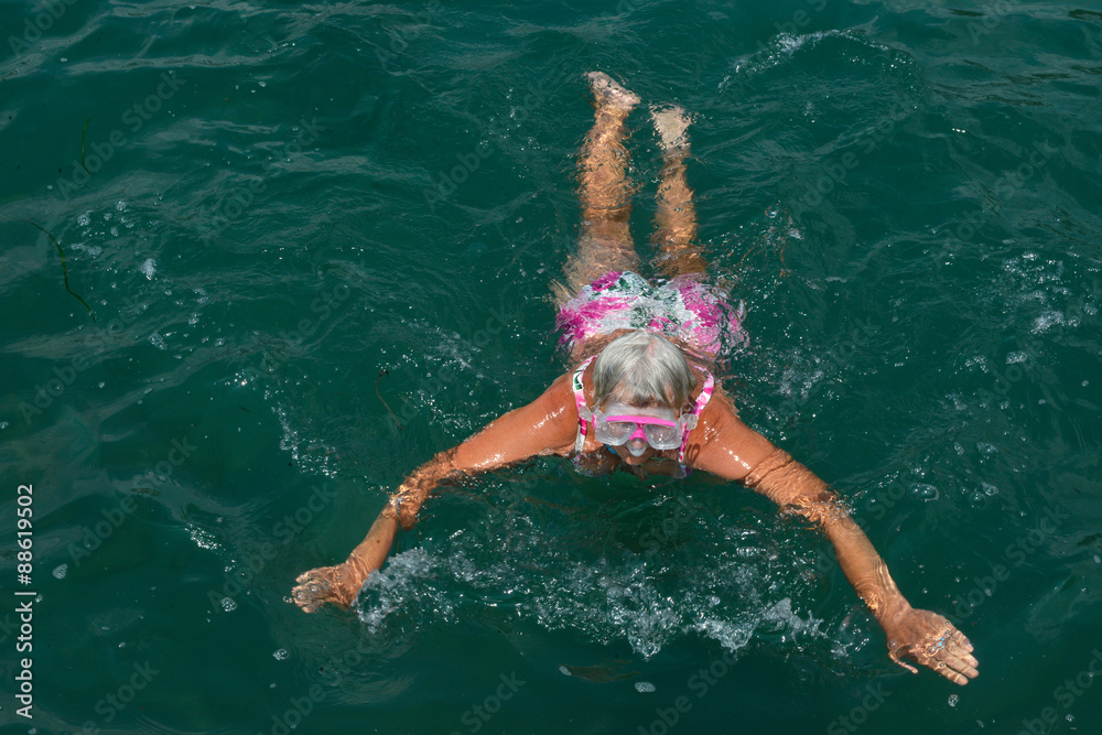 Aged woman is swimming with goggles in the sea.