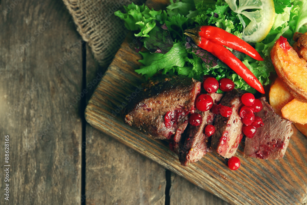 Beef with cranberry sauce, roasted potato slices on cutting board, on wooden background