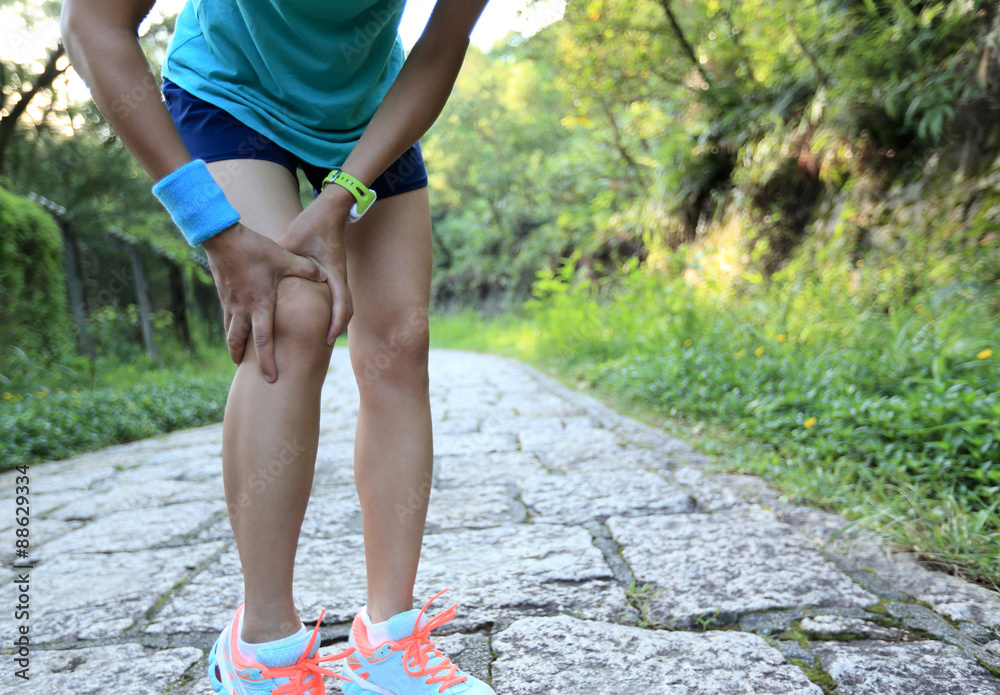 woman runner hold sports injured knee on forest trail. 
