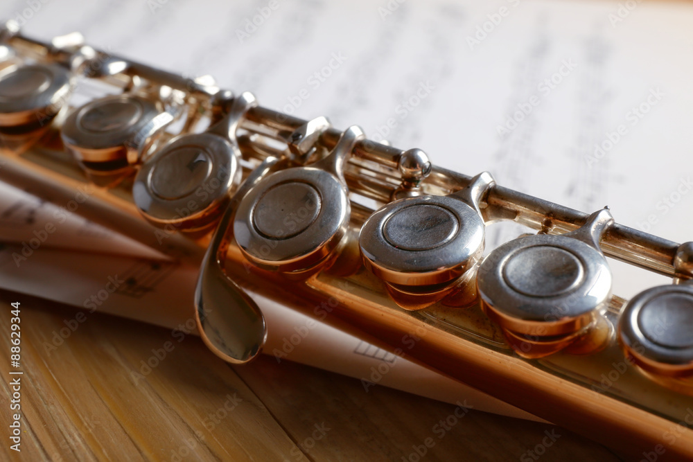 Naklejka premium Silver flute with music notes on wooden table close up