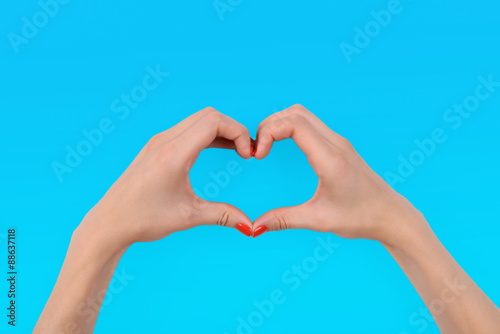 Young woman makes heart using fingers on light background