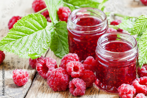 Quadro su tela Two jars of raspberry jam, fresh berries and green leaves in an