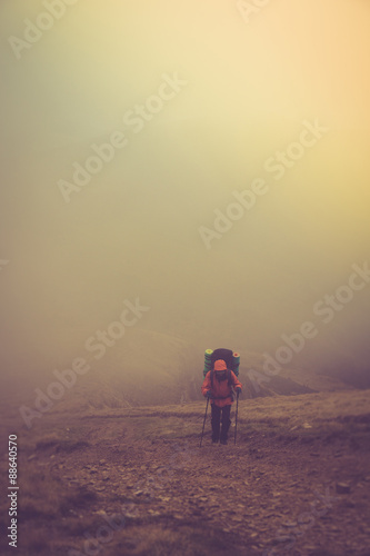 Tourists with backpacks climb to the top of the mountain in fog.