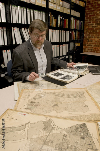 Researcher in archive, searching through maps and photographs.