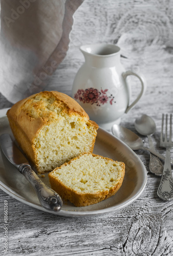 simple cake on an oval plate, milk jug and silver cutlery on a light wooden background