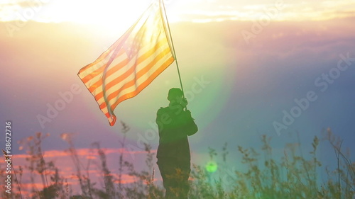 Soldier waves  American flag against   sunset sky. Slow motion scene