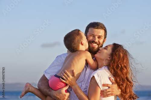 Portrait of positive family - happy mother and father holding baby son on hands walk with fun on sand sea beach. Active parents and people outdoor activity on tropical summer holidays with children