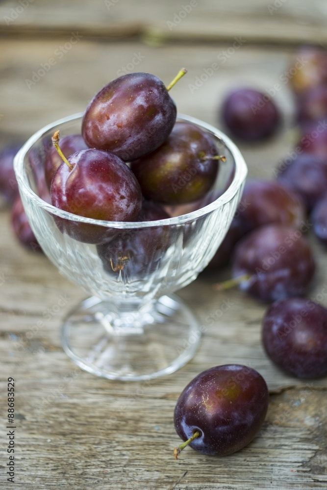 Vase of purple plums on wooden background, purple food Vase of purple plums on wooden background, purple food
