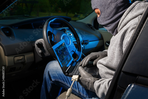 Car thief stealing a car. Starting the car with a lap top