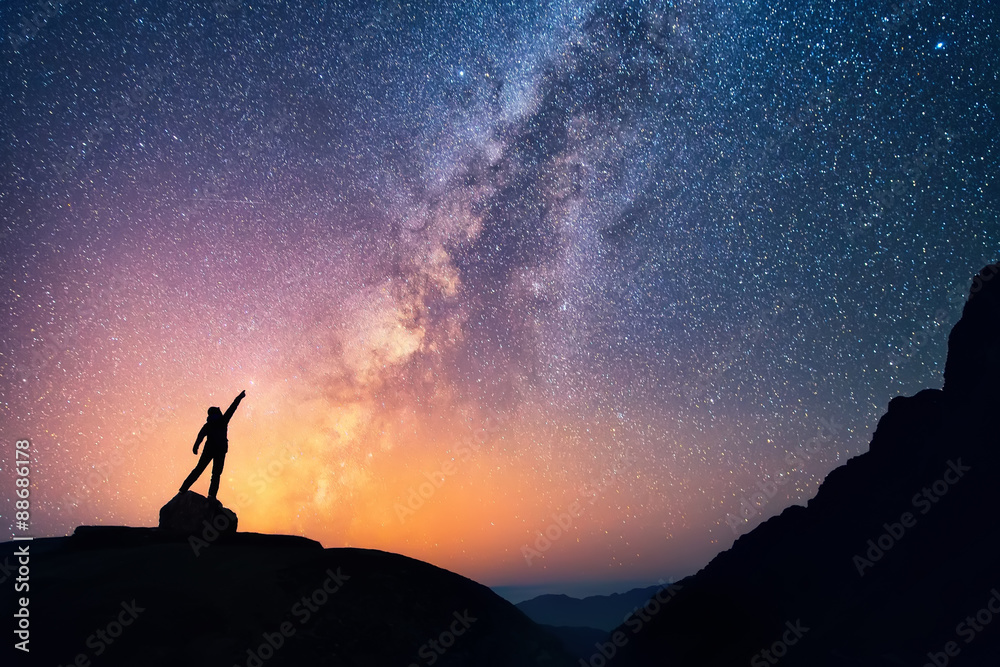 Catch the star. A person is standing next to the Milky Way galaxy pointing on a bright star. - obrazy, fototapety, plakaty 