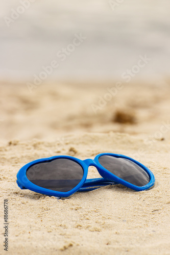 Blue sunglasses shaped heart on the sand