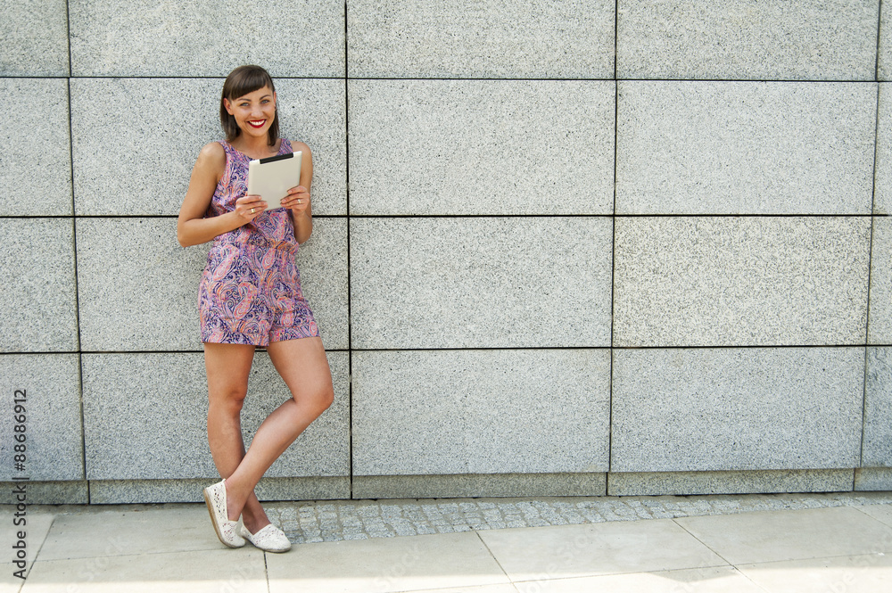 Young woman using tablet standing against the wall in the city s Young woman using tablet standing against the wall in the city s