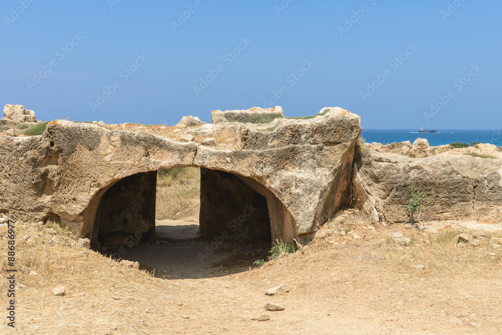 Entrance to an ancient stone burial tomb with Mediterranean Sea in the background at an archaeological site in Paphos, Cyprus.