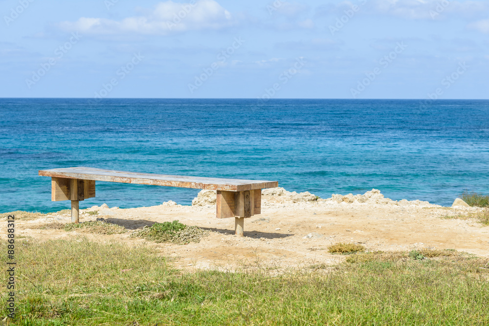 Wooden bench overlooking the blue waters of the Mediterranean Sea in Paphos, Cyprus.