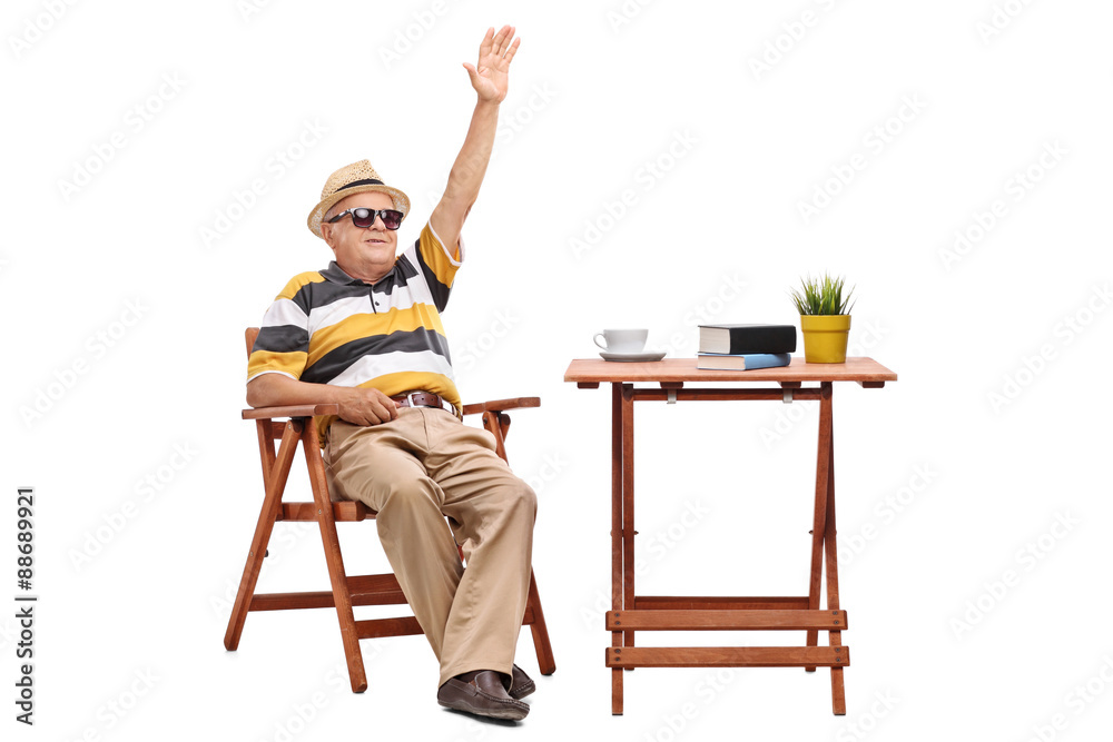 Senior man sitting at a table and waving with hand Senior man sitting at a table and waving with hand