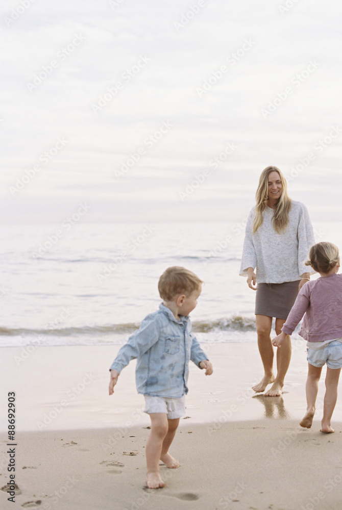 Woman playing with her son and daughter on a sandy beach by the ocean. Woman playing with her son and daughter on a sandy beach by the ocean.