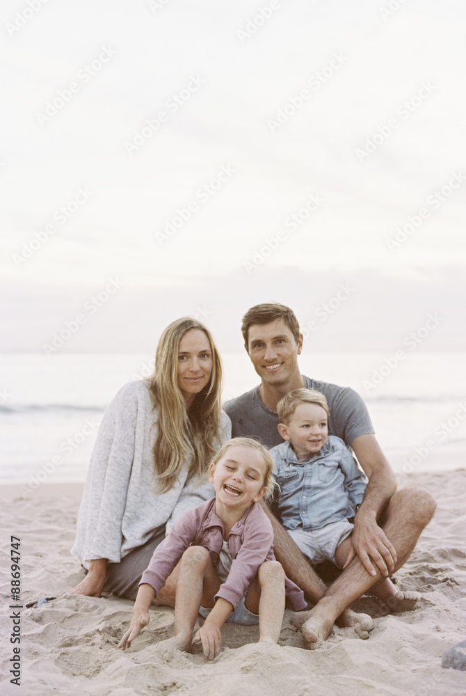 Couple sitting with their son and daughter on a sandy beach by the ocean, looking at camera, smiling. Couple sitting with their son and daughter on a sandy beach by the ocean, looking at camera, smiling.