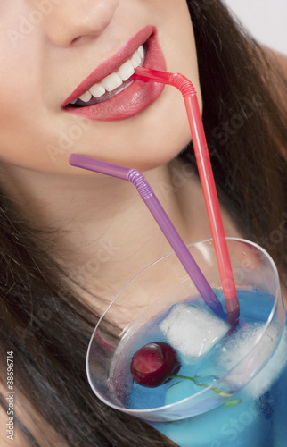 Close-up of a young woman drinking blue cocktail with ice and cherry