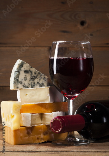 Red wine with various types of cheese on wooden background