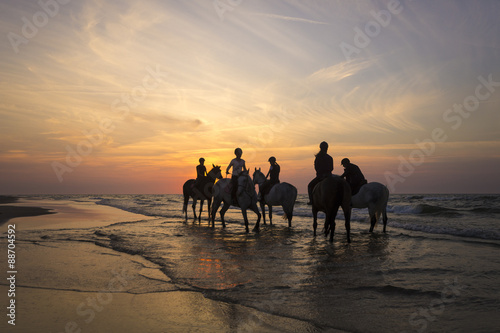 Jeźdźcy na koniach jadący brzegiem morza o zachodzie słońca © Mike Mareen