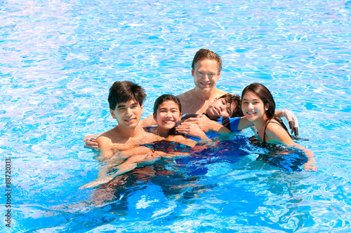 Multiracial family swimming together in pool. Disabled youngest